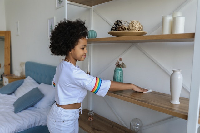 Young teen cleaning a brown wooden shelf in an apartment